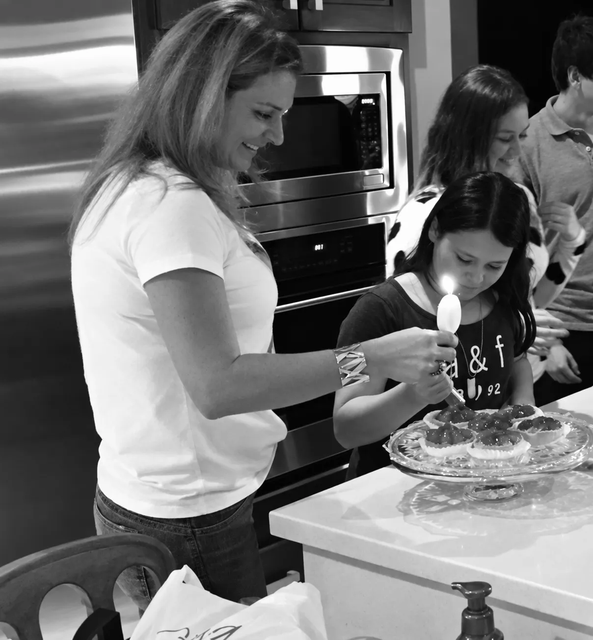 En blanco y negro, una mamá y su hija en la cocina, encendiendo una vela sobre unas tartaletas