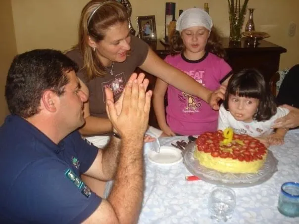 Foto familiar: una niña frente a su pastel de cumpleaños con fresas, rodeada de su familia